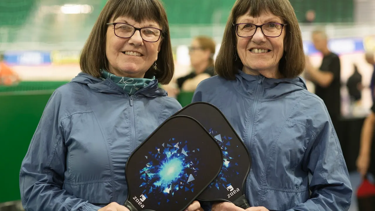 Two smiling women hold pickleball paddles.